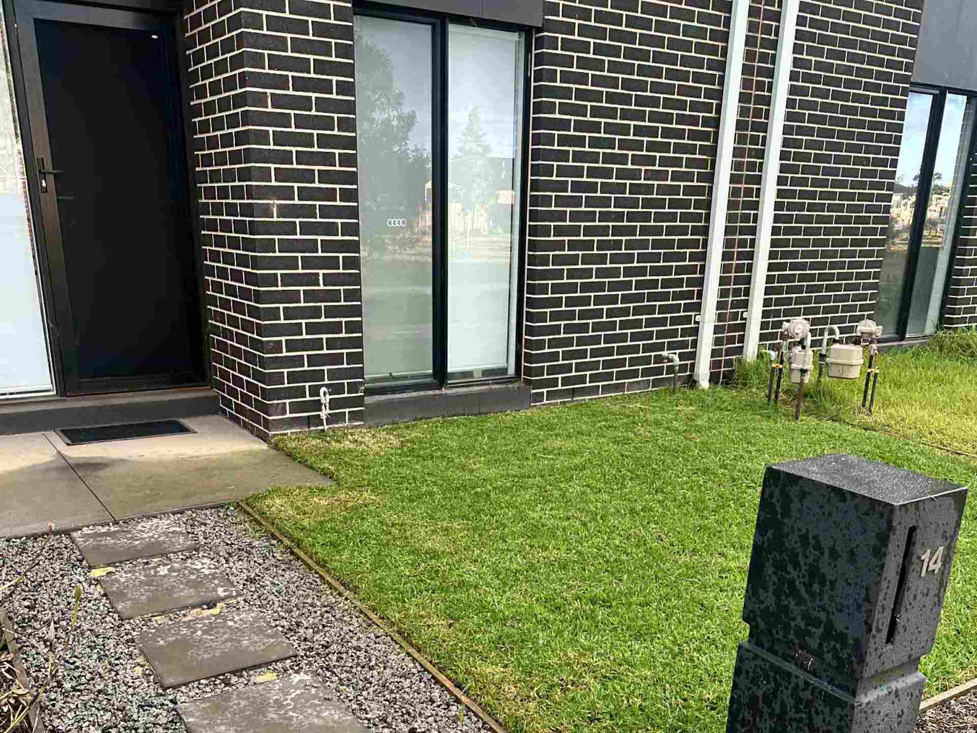 Neat front lawn and stepping-stone gravel path at a dark brick townhouse